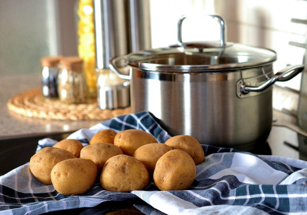 A pan with a lid on and a tea towel with potatoes resting on them near the stove. This image shows a potential fire hazard if the tea towel were to set on fire.